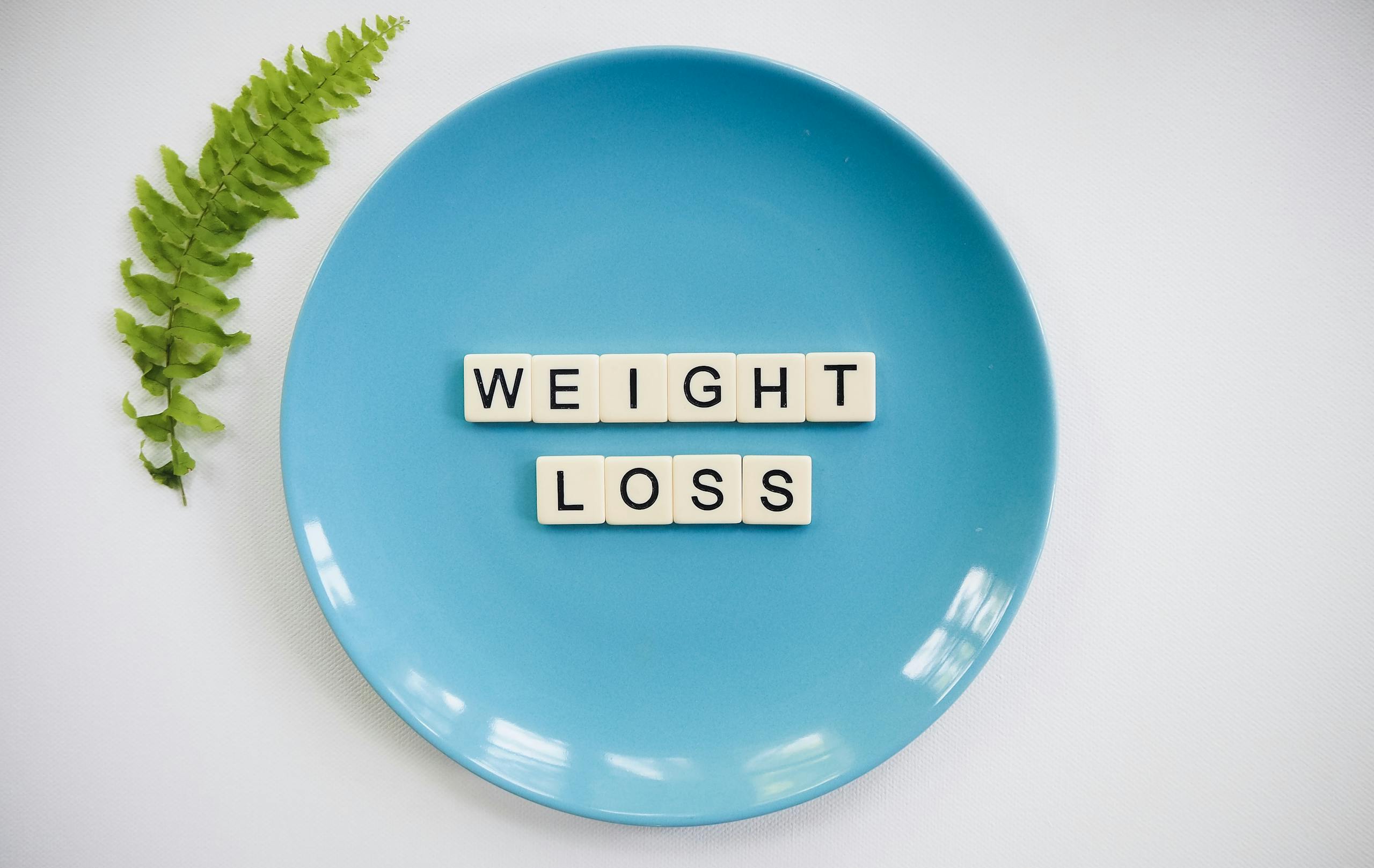 A blue plate with 'weight loss' tiles and a fern leaf on white background.