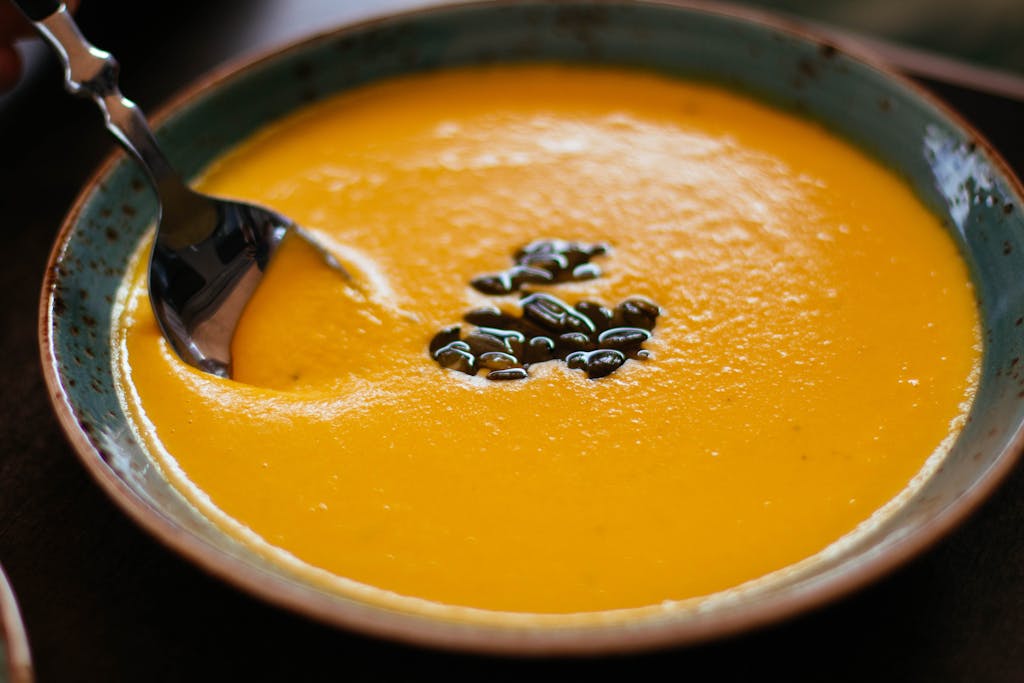 Close-up of creamy pumpkin soup with seeds in a blue ceramic bowl, perfect for a warm fall meal. unmotivated food