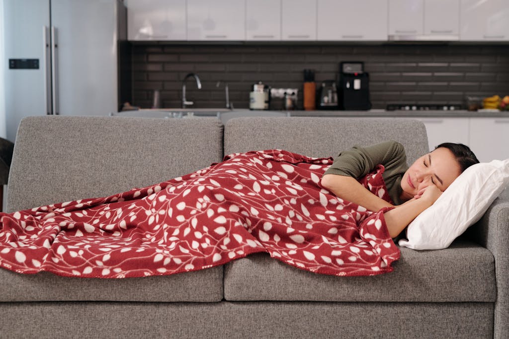 Woman peacefully napping on a couch with a red patterned blanket in a modern kitchen setting.