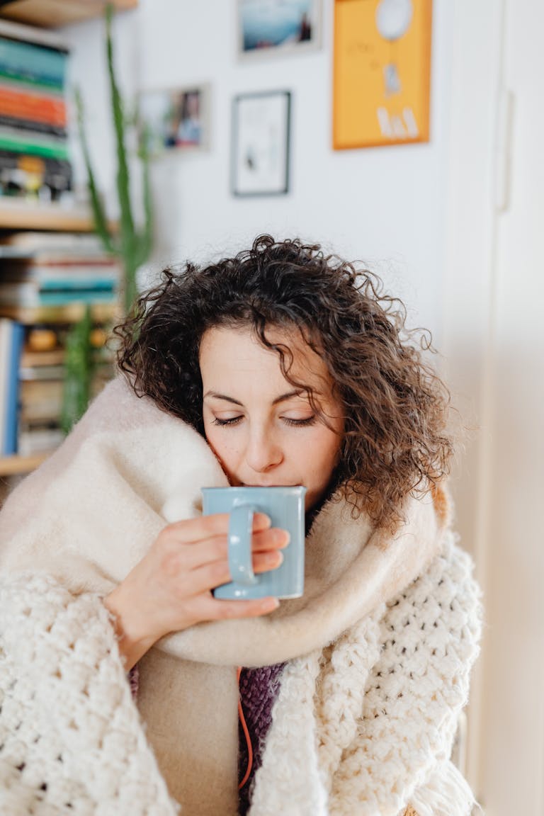 Woman wrapped in a warm scarf enjoying a hot drink, capturing a peaceful cozy indoor moment.