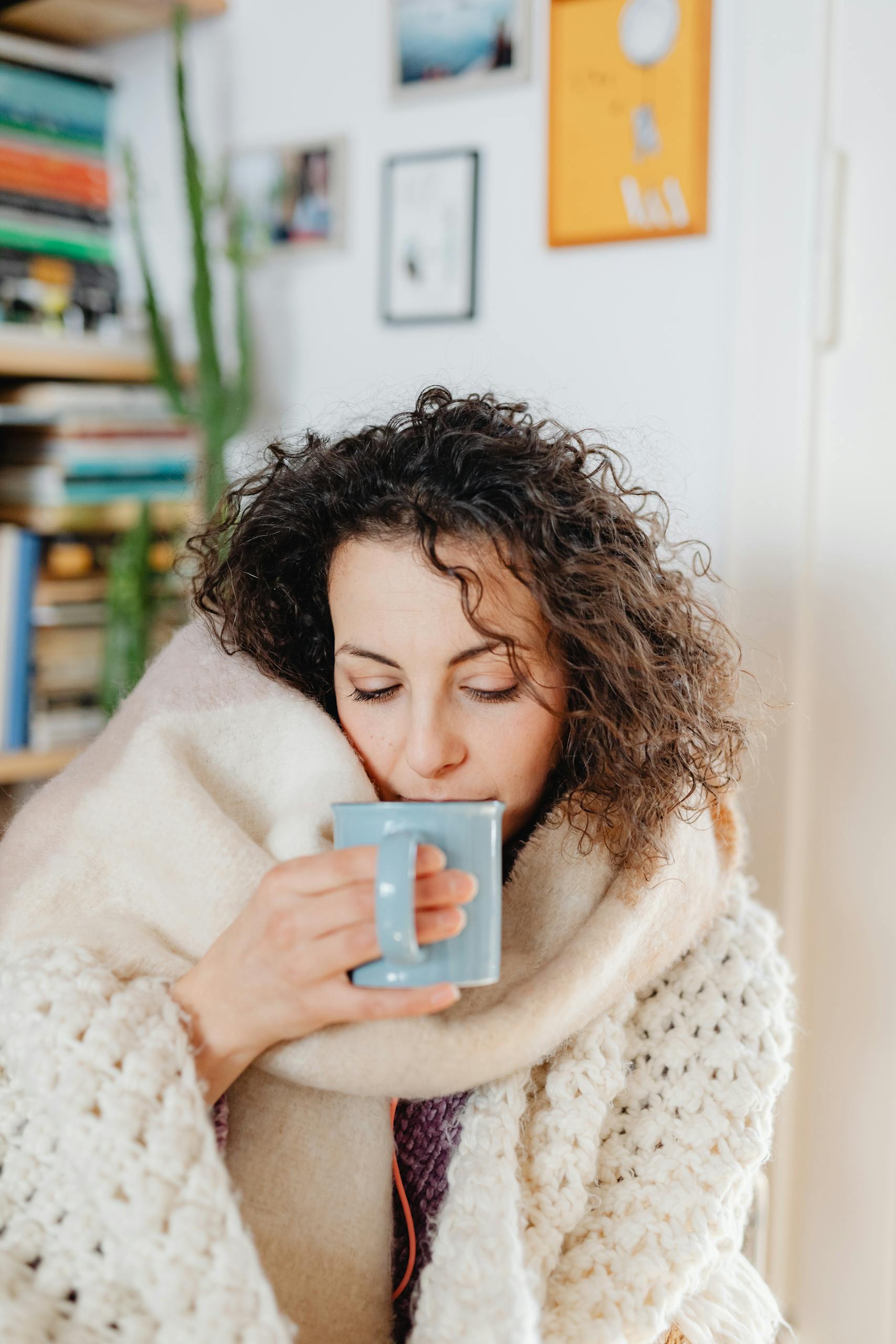 Woman wrapped in a warm scarf enjoying a hot drink, capturing a peaceful cozy indoor moment.