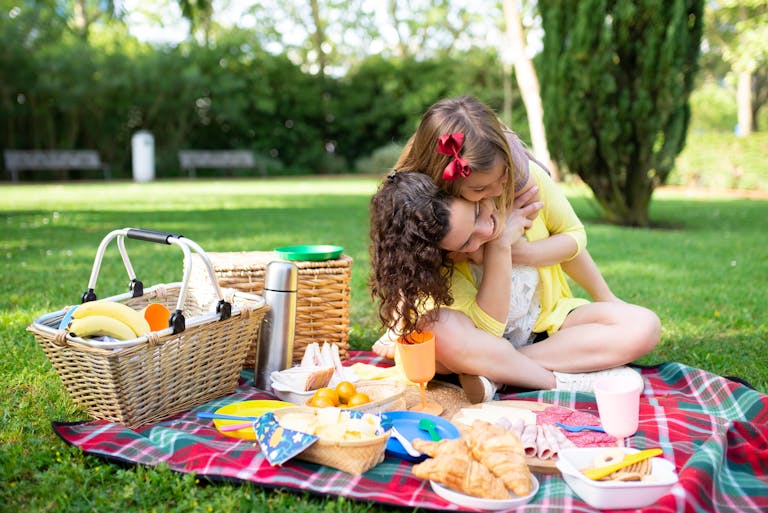 A mother and daughter share a loving embrace on a picnic, surrounded by food and nature. honouring hunger