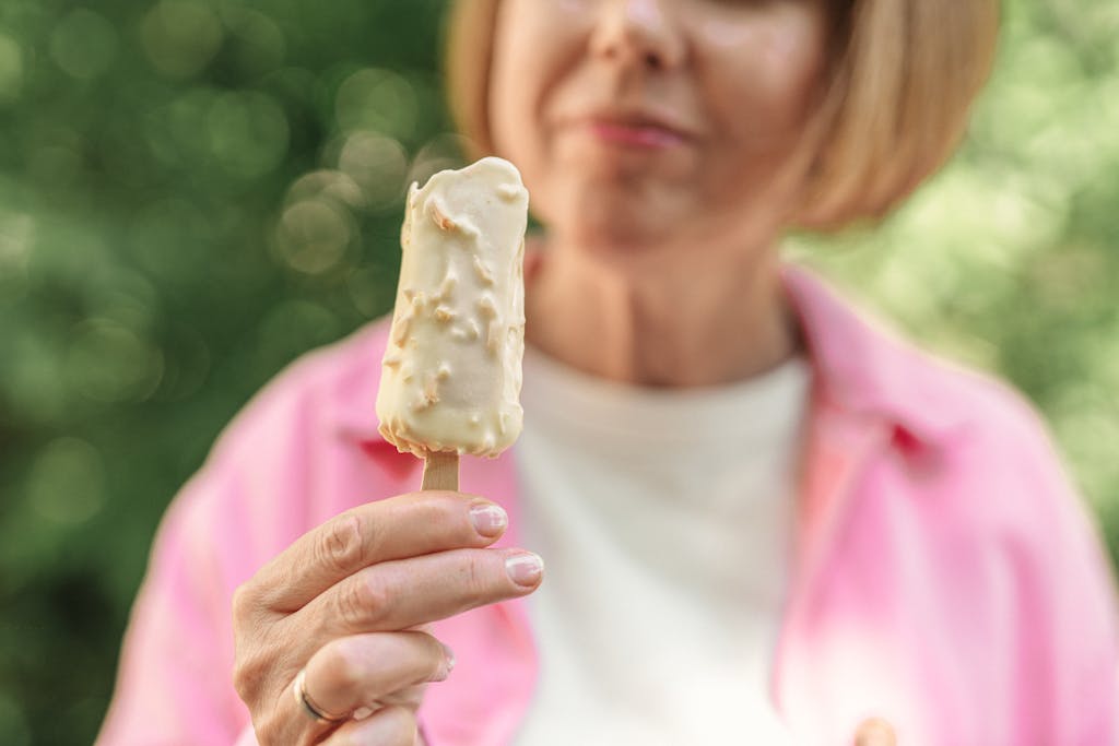 Elderly woman honouring her hunger holding a delicious vanilla ice pop with a joyful expression outdoors.