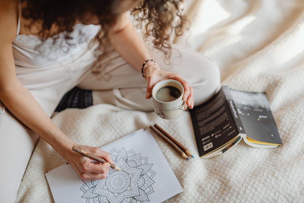 Woman colouring mandala while holding coffee on cozy blanket, during autumn, symbolizing rest and calm